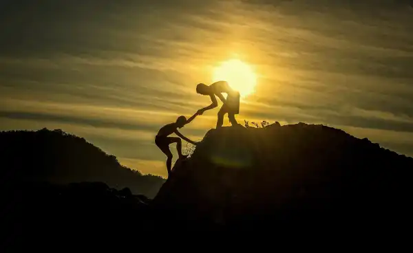 Silhouette of two people offering a hand on a hill at sunset